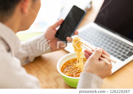 A middle-aged man eating cup ramen while working in the office A middle-aged man eating cup ramen while working in the office 126228267
