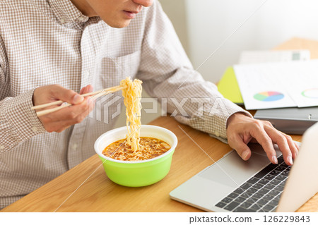 A middle-aged man eating cup ramen while working in the office 126229843