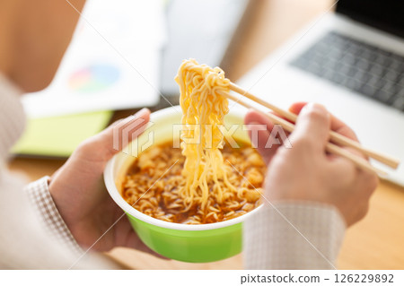 一位中年男子在辦公室工作時吃杯拉麵 一位中年男子在辦公室工作時吃杯拉麵 126229892