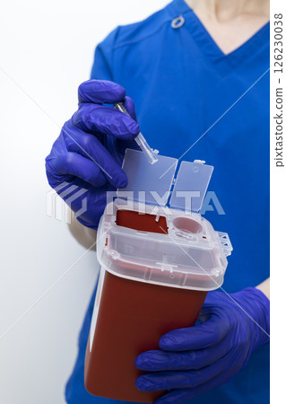 Doctor Disposes Needle, Ampule In Sharps Container. Disposal Container For Infectious Waste, Reducing Medical Waste Disposal. Small Medical Waste Plastic Box With Sharps For Bio Hazard. Vertical Plane Doctor Disposes Needle, Ampule In Sharps Container. Disposal Container For Infectious Waste, Reducing Medical Waste Disposal. Small Medical Waste Plastic Box With Sharps For Bio Hazard. Vertical Plane 126230038