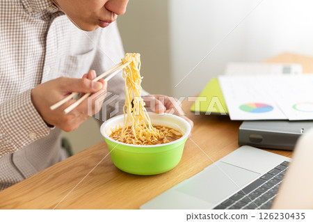 一位中年男子在辦公室工作時吃杯拉麵 一位中年男子在辦公室工作時吃杯拉麵 126230435