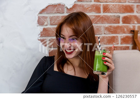 Woman smiling with green smoothie in cozy modern cafe 126230557