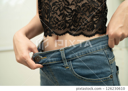 Young Asian woman losing weight wearing loose pants in oversize jeans. 126230610