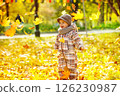 Happy child is throwing heap of maple leaves at golden autumn park background. 126230987