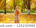 Happy child is holding heap of maple leaves at golden autumn park background. 126230988