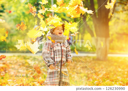 Happy child is throwing heap of maple leaves at golden autumn park background. Happy child is throwing heap of maple leaves at golden autumn park background. 126230990