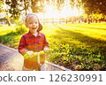 Happy little boy is riding scooter and smiling at summer sunny park background. 126230991