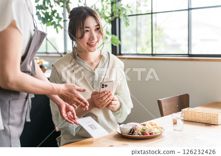 一名服務生在咖啡館出示二維碼，一名女顧客正在操作智慧型手機 126232426