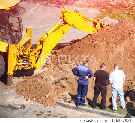 Workers stand near a pit with a loader with sand and emergency services in the background. Sewer leak repair, gas service, Close-up 126232921