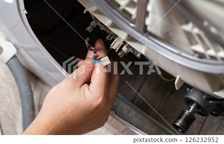 The hand of the master removes the electrical chips to remove the heating element of the washing machine and the heating sensor. Repair of washing machines, industry 126232952