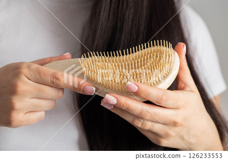 Girl holding massage comb on black hair background. Wet and tangled hair care, close-up. Hair care 126233553