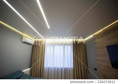Beautiful designer stylish stretch ceiling with LED light lines against the background of a window with curtains in the living room. Option for lighting with light lines. Beautiful designer stylish stretch ceiling with LED light lines against the background of a window with curtains in the living room. Option for lighting with light lines. 126233612