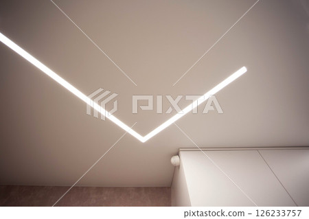 Modern designer stretch ceiling with illuminated LED lines in the room, backlighting Modern designer stretch ceiling with illuminated LED lines in the room, backlighting 126233757