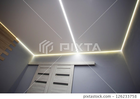 Beautiful modern stretch ceiling with yellow LED lines around the perimeter. Designer stylish ceiling in the hall. Beautiful modern stretch ceiling with yellow LED lines around the perimeter. Designer stylish ceiling in the hall. 126233758