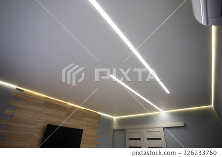 Beautiful modern stretch ceiling with yellow LED lines around the perimeter. Designer stylish ceiling in the hall. Beautiful modern stretch ceiling with yellow LED lines around the perimeter. Designer stylish ceiling in the hall. 126233760