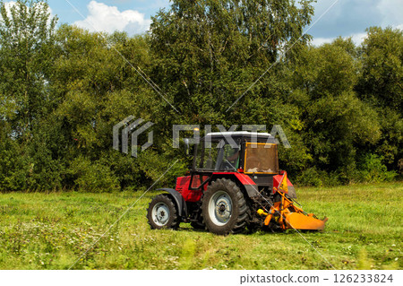 Roadside mowing of grass with a tractor near the road. Mowing roadsides, maintaining roadside areas, copy space for text. Road maintenance organization 126233824