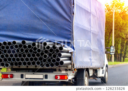Transportation of metal pipes in a truck on a road in summer against the backdrop of the sun, industry. Transport company that provides metal transportation services, close-up 126233826
