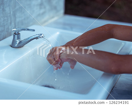 Child washing hands. Close-up of hands being cleaned at a public faucet. 126234191