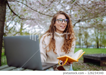 Beautiful female student is using laptop, notepad to prepare for outdoor classes. Education concept. Beautiful female student is using laptop, notepad to prepare for outdoor classes. Education concept. 126234340