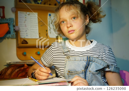 Teen Girl Writing at Desk with Thoughtful Expression 126235098
