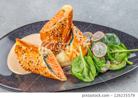 Salmon fillet on leek, baked in puff pastry with creamy sauce and salad. Salmon Wellington 126235579