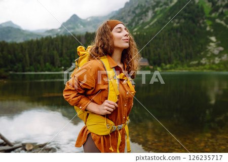 Travel Slovakia, Europe. Tourist with a yellow backpack stands against the backdrop of alpine lake. 126235717