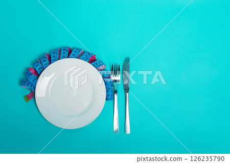 Healthy eating weight loss fitness. Empty plate with fork knife measuring tape in centimeters on a blue background from above. Diet menu Obesity. Place for an inscription. Advertising. 126235790