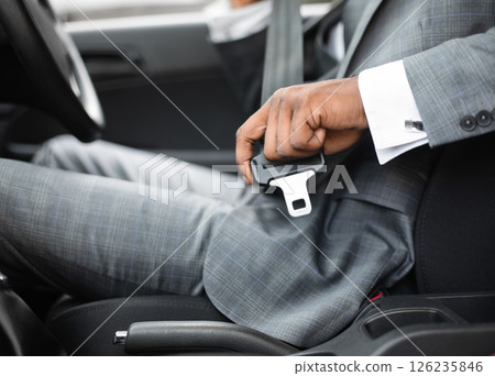 Driving safety concept. Unrecognizable black businessman fasten seat belt in his car, ready to go to office. African american man in stylish suit putting on his seatbelt before driving car, cropped 126235846