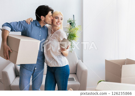 Moving House Concept. Man Kissing Woman Holding Box Unpacking In New House. Free Space For Text Moving House Concept. Man Kissing Woman Holding Box Unpacking In New House. Free Space For Text 126235866