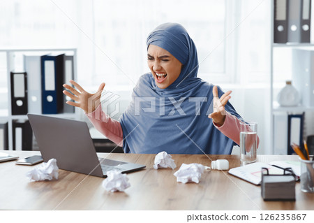 Deadline Concept. Stressed Arabic Businesswoman Looking At Laptop Screen And Raising Hands In Fury, Having Problems At Work Deadline Concept. Stressed Arabic Businesswoman Looking At Laptop Screen And Raising Hands In Fury, Having Problems At Work 126235867