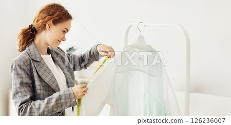 Young dressmaker measuring shirt sleeve with measuring tape, working in tailoring atelier 126236007