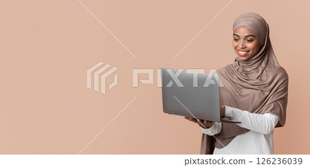 Freelance Job Concept. Afro Muslim Woman In Hijab Using Laptop, Working Online, Standing Over Yellow Background In Studio, Copy Space Freelance Job Concept. Afro Muslim Woman In Hijab Using Laptop, Working Online, Standing Over Yellow Background In Studio, Copy Space 126236039