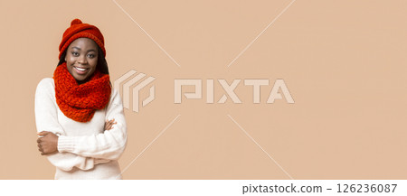 A cheerful young African American woman stands confidently with her arms crossed, dressed in a warm, fluffy sweater and a vibrant red scarf and hat, copy space A cheerful young African American woman stands confidently with her arms crossed, dressed in a warm, fluffy sweater and a vibrant red scarf and hat, copy space 126236087