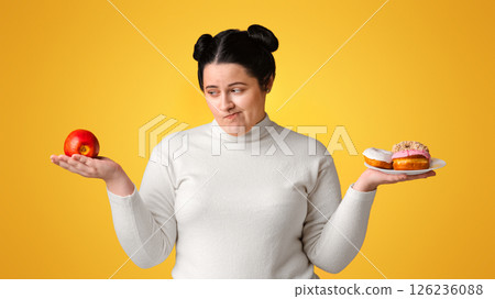Complex Choice. Hungry Obese Girl On Diet Making Choice Between Donuts And Apple, Standing Over Yellow Background In Studio, Free Space Complex Choice. Hungry Obese Girl On Diet Making Choice Between Donuts And Apple, Standing Over Yellow Background In Studio, Free Space 126236088