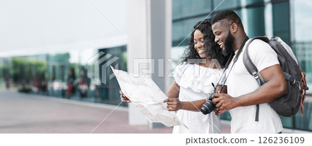 African American couple looks at a map while standing outside a modern building, they are both smiling and enjoying their time together. They appear to be on a vacation or traveling for pleasure. 126236109