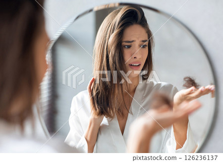 Hairloss Concept. Worried Young Woman Holding Bunch Of Fallen Hair In Hand While Standing Near Mirror In Bathroom, Stressed Beautiful Lady Suffering Alopecia Or Health Problems, Selective Focus Hairloss Concept. Worried Young Woman Holding Bunch Of Fallen Hair In Hand While Standing Near Mirror In Bathroom, Stressed Beautiful Lady Suffering Alopecia Or Health Problems, Selective Focus 126236137