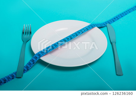 Healthy food, fitness for weight loss. An empty plate with a forkknife measuring tape in centimeters on a blue background from above. Diet menu Obesity. Place for an inscription. Advertising. 126236160