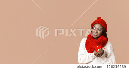 Interested african american winter woman enjoying hot tea or coffee, holding red mug, looking at copy space, beige background, panorama 126236289