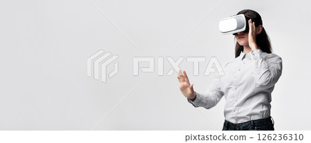 A woman wearing a virtual reality headset, extending her hand out, seemingly interacting with something in the virtual world. A woman wearing a virtual reality headset, extending her hand out, seemingly interacting with something in the virtual world. 126236310