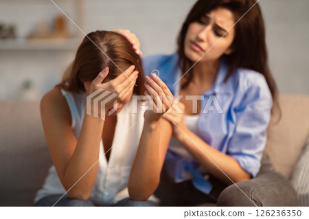 Divorce Concept. Friend Comforting Desperate Girl After Breakup With Ex-Husband Holding Ring Sitting On Couch At Home. Divorce Concept. Friend Comforting Desperate Girl After Breakup With Ex-Husband Holding Ring Sitting On Couch At Home. 126236350