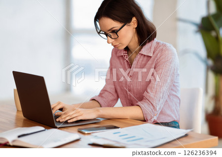 Home Office. Portrait of young woman in eyewear using laptop, working remotely, free space Home Office. Portrait of young woman in eyewear using laptop, working remotely, free space 126236394