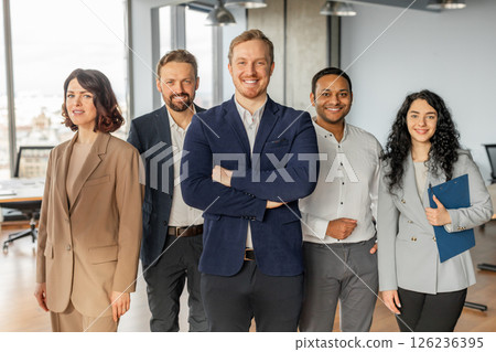 A diverse group of five business professionals stand together in a modern office setting. They are all wearing business attire and appear confident and successful. A diverse group of five business professionals stand together in a modern office setting. They are all wearing business attire and appear confident and successful. 126236395