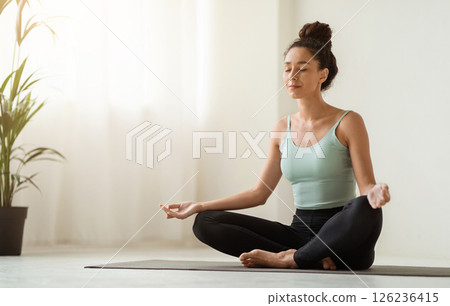Morning Meditation. Beautiful Calm Woman Meditating At Home In Lotus Position, Peaceful Young Brunette Lady Practicing Yoga, Sitting With Closed Eyes On Fitness Mat In Light Room, Copy Space 126236415