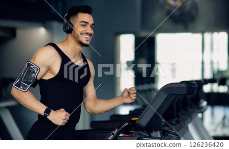 Handsome Young Muscular Arab Man In Wireless Headphones Jogging On Treadmill At Gym, Sporty Motivated Middle Eastern Guy Listening Music While Running, Enjoying Making Sports, Copy Space Handsome Young Muscular Arab Man In Wireless Headphones Jogging On Treadmill At Gym, Sporty Motivated Middle Eastern Guy Listening Music While Running, Enjoying Making Sports, Copy Space 126236420
