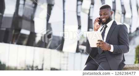Positive African Entrepreneur Talking On Cellphone Using Digital Tablet During Coffee Break In City Urban Area 126236477
