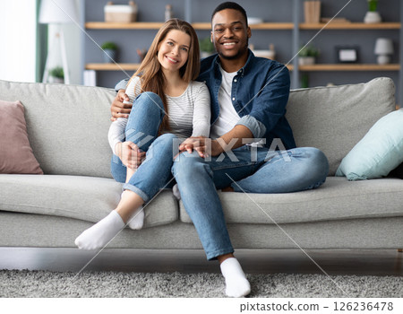 Portrait Of Happy Young Interracial Spouses Posing On Couch At Home, Cheerful Mixed Couple Black Man And White Woman Embracing On Sofa While Relaxing In Cozy Living Room Together, Free Space 126236478