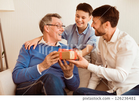 Grandfather's Birthday. Mature Son And Grandson Congratulating Grandpa Giving Him Gift Sitting On Couch At Home. Selective Focus 126236481
