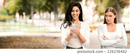 Envy Concept. Jealous Girl Looking At Friend's Phone Walking Together Outdoors At Park. Selective Focus 126236482