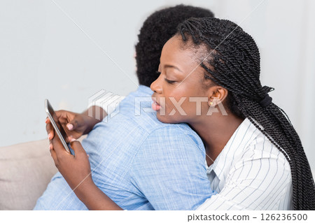 Cheating wife. Young black woman texting on cellphone with somebody while embracing her husband at home, closeup Cheating wife. Young black woman texting on cellphone with somebody while embracing her husband at home, closeup 126236500