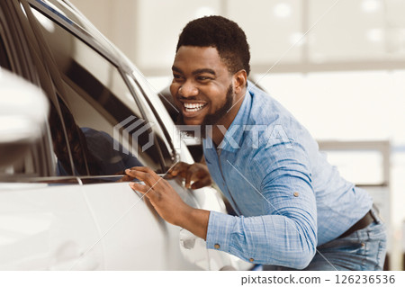 Happy Car Owner. African Guy Touching His New Vehicle Excited About Buying Automobile In Dealership Showroom. Selective Focus Happy Car Owner. African Guy Touching His New Vehicle Excited About Buying Automobile In Dealership Showroom. Selective Focus 126236536